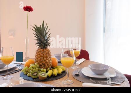 Ein Esstisch aus Eiche Mit einem Teller mit verschiedenen frischen Früchten und Gläsern mit Orangensaft Stockfoto