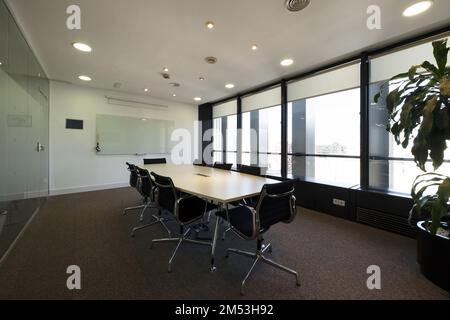 Sitzungssaal mit langem Holztisch mit schwarzen Drehstühlen und Wand mit Fenstern Stockfoto