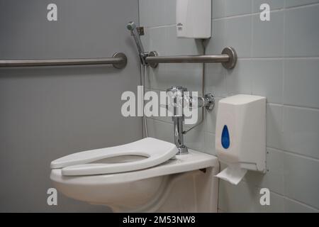 Schule, Universität oder öffentliche Behindertentoilette, weiße Toilette mit Waschwerkzeug oder 'Shattaf' und Mülleimer. Arabische Toilette mit Waschspray, modernes Toi Stockfoto