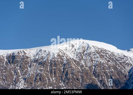 Schneebedeckte Berggipfel, die im Winter von der Sonne beleuchtet werden Stockfoto