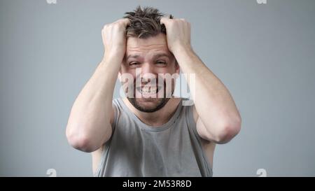 Der junge Mann ist gereizt, er reißt sich die Haare auf dem Kopf unter Stress Stockfoto