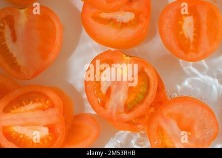 Tomatenscheiben im Wasser auf weißem Hintergrund. Tomaten-Nahaufnahme in Flüssigkeit mit Blasen. Scheiben roter reifer Tomaten im Wasser. Makrobild von Gemüse in Stockfoto