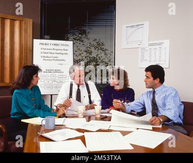 Geschäftsleute und Geschäftsfrauen, die am Konferenztisch sitzen und Arbeitsthemen diskutieren, Unterlagen auf dem Tisch, Staffelei im Hintergrund Stockfoto