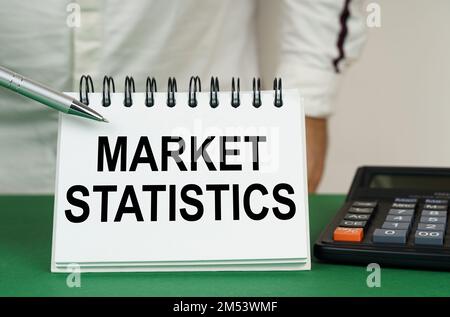 Geschäftskonzept. Auf einer grünen Oberfläche befindet sich ein Taschenrechner, ein Mann zeigt mit einem Stift auf ein Notizbuch mit der Aufschrift Marktstatistik Stockfoto