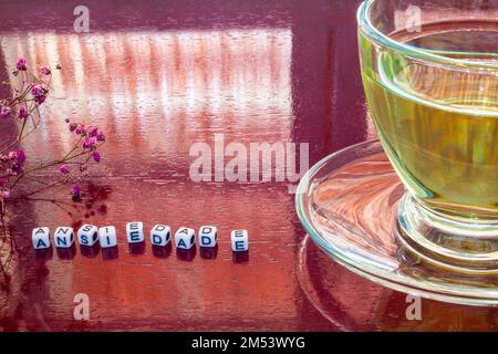 Goiania, Goiás, Brasilien – 25. Dezember 2022: Detail eines Glasbechers mit Tee auf dem glänzenden Tisch mit dem Wort „Angst“ mit Stücken und Blumen Stockfoto