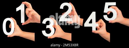Kinderhände halten Zahlen. Ein Satz weißer Zahlen in der Hand auf schwarzem isoliertem Hintergrund. Null, eins, zwei, drei, vier, Fünf. Stockfoto