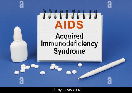 Medizinisches Konzept. Auf blauem Hintergrund ein Stift, Tabletten und ein Notizblock mit der Aufschrift "AIDS Acquired Immunodeficiency Syndrome" Stockfoto