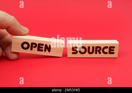 Geschäftskonzept. Auf rotem Hintergrund, Holzblöcke, einer davon in der Hand. Die Blöcke sind geschrieben - OPEN SOURCE Stockfoto