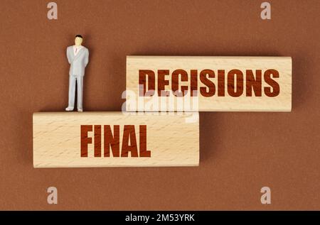 Geschäftskonzept. Auf einer braunen Oberfläche auf Holzblöcken mit der Aufschrift "endgültige Entscheidungen" befindet sich eine Miniaturfigur eines Geschäftsmannes. Stockfoto