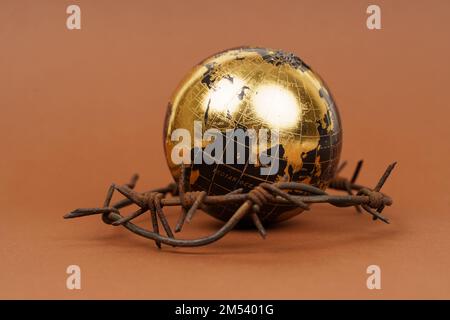 Der Begriff der Symbolik. Auf einer braunen Oberfläche befindet sich eine Kugel, die von Stacheldraht umgeben ist. Stockfoto