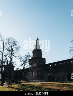 Ein kleiner vertikaler Blick auf das Castel Sforzesco in Mailand, Italien, während des Sonnenuntergangs, umgeben von bläulichen Bäumen im Winter Stockfoto