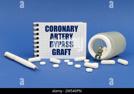 Medizinisches Konzept. Auf einer blauen Oberfläche ist ein Glas Pillen, eine Figur eines Mannes, ein Notizblock mit der Aufschrift - Koronararterien-Bypass-Transplantat Stockfoto