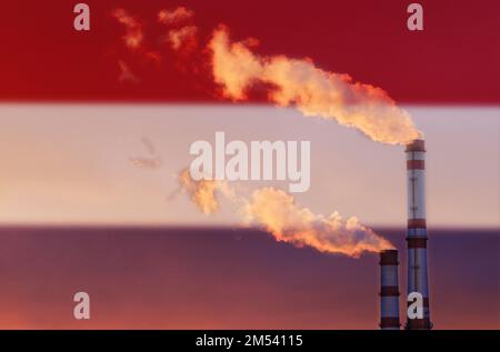 Ökologisches Konzept. Vor dem Hintergrund der Flagge der Niederlande strömt Rauch aus den Kamin eines Industrieunternehmens und verschmutzt die Stockfoto