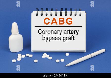 Medizinisches Konzept. Auf blauem Hintergrund einen Stift, Tabletten und einen Notizblock mit der Aufschrift „CABG koronarer Bypass“ Stockfoto