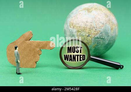 Geschäftskonzept. Auf einer grünen Oberfläche befinden sich eine Kugel, eine Hand und eine Lupe mit der Inschrift - Most Wanted Stockfoto