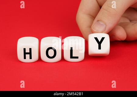 Geschäftskonzept. Auf rotem Hintergrund bewegt die Hand einer Person die Würfel mit der Inschrift "Heilig" Stockfoto