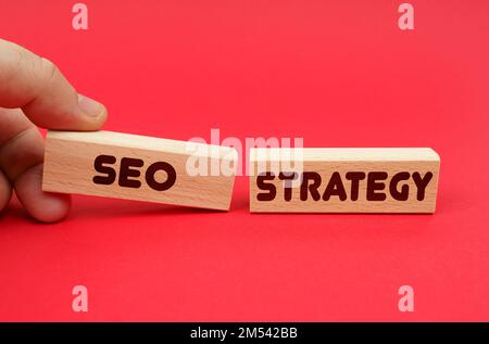 Geschäftskonzept. Auf rotem Hintergrund, Holzblöcke, einer davon in der Hand. Die Blöcke sind geschrieben - SEO-STRATEGIE Stockfoto