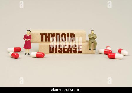 Medizinisches Konzept. Neben den Miniaturfiguren der Menschen sind Tabletten und Holzblöcke mit der Inschrift - Schilddrüsenerkrankung Stockfoto