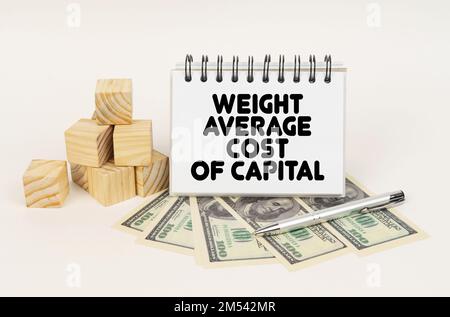 Geschäftskonzept. Auf einer weißen Oberfläche, Würfel, Dollars, ein Stift und ein Notizblock mit der Inschrift - DURCHSCHNITTLICHES KAPITALGEWICHT Stockfoto