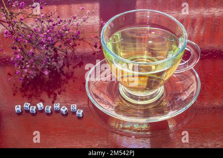 Goiania, Goiás, Brasilien – 25. Dezember 2022: Eine Glasbecher mit Tee auf dem glänzenden Tisch, mit dem Wort "Angst" mit Stücken und Blumen. Stockfoto