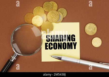 Geschäftskonzept. Auf einer braunen Oberfläche befinden sich Münzen, ein Stift, eine Lupe und Aufkleber mit der Aufschrift „Sharing Economy“ Stockfoto