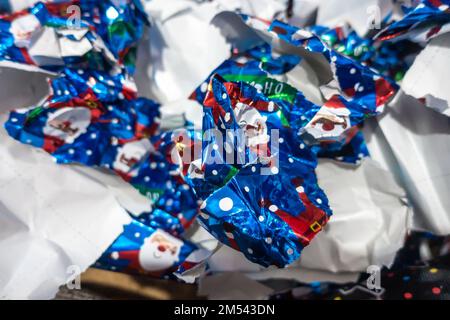 Weggeworfenes Weihnachts-Geschenkpapier, das in einen großen Stapel auf den Boden geworfen wurde und von Geschenken gerissen wurde. Stockfoto