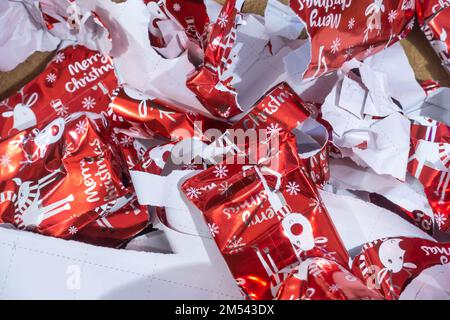 Weggeworfenes Weihnachts-Geschenkpapier, das in einen großen Stapel auf den Boden geworfen wurde und von Geschenken gerissen wurde. Stockfoto