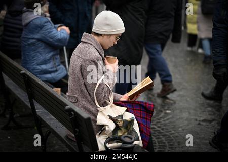 Eine junge Frau mit einem Becher wird am 25. Dezember 2022 auf dem Altstädter Ring in Warschau, Polen, beim Lesen eines Buches gesehen. Stockfoto