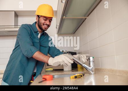 Lächelnder Klempner repariert Wasserhahn in der Küche des Kunden. Guter Service für die Sanitäranlagen Stockfoto