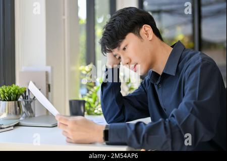 Seitenansicht eines jungen, gutaussehenden Geschäftsmannes konzentriert sich auf sein Dokument, während er im Büro arbeitet Stockfoto