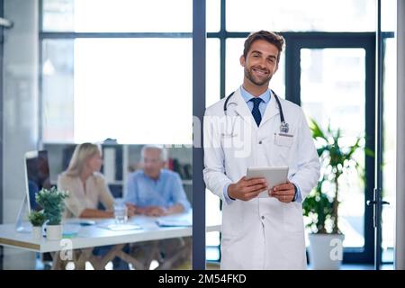 Es ist eine Möglichkeit, schnell auf alle meine Krankenakten zuzugreifen. Porträt eines Arztes mit einem digitalen Tablet mit zwei im Hintergrund sitzenden Patienten. Stockfoto