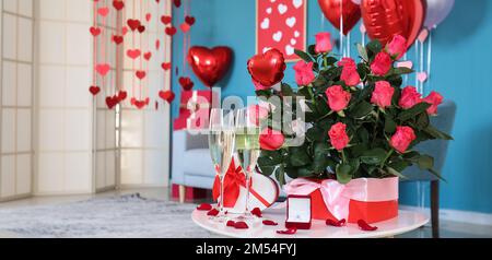 Geschenk mit Verlobungsring, Gläsern Champagner und frischen Rosen auf dem Tisch im Zimmer, dekoriert zum Valentinstag Stockfoto