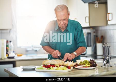 Ruhestandsleben vom Feinsten. Ein älterer Mann, der zu Hause in seiner Küche zu Mittag isst. Stockfoto