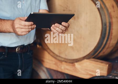 Erfahren Sie alles, was Sie über Wein wissen müssen, online. Ein unerkannter männlicher Sommelier, der sein digitales Tablet bei der Arbeit benutzt. Stockfoto