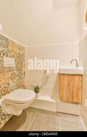 Ein Badezimmer mit künstlerischem Design auf der Tapete und die Toilette im Zimmer ist weiß, beige und orange Stockfoto