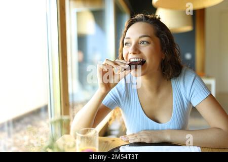Glückliche Frau, die Schokoladenkuchen isst, sitzt in einem Restaurant Stockfoto
