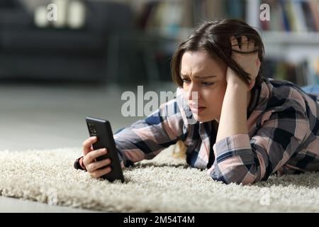 Trauriger Teenager, der nachts zu Hause sein Smartphone auf dem Boden überprüft Stockfoto