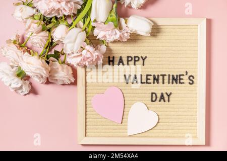 „Happy Valentine's Day“-Schriftzug auf dem Brieftafel und wunderschöne Frühlingsblumen auf hellrosa Hintergrund. Valentinstag, Frauentag, Muttertag Greeti Stockfoto