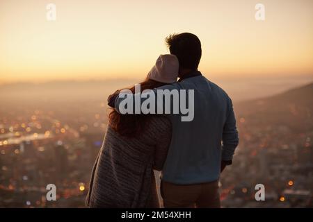 Der frühe Vogel fängt den Sonnenaufgang. Rückblick auf ein liebevolles junges Paar, das bei Tagesanbruch die Aussicht auf die Stadt bewundert. Stockfoto