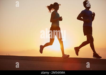 Jedes Workout zählt. Ein Paar mit Silhouetten, das bei Sonnenaufgang laufen will. Stockfoto