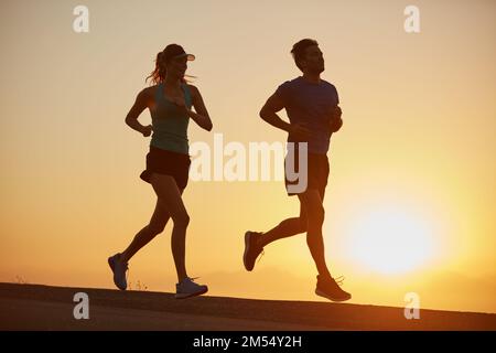 Bleiben Sie ruhig und joggen Sie weiter. Ein Paar mit Silhouetten, das bei Sonnenaufgang laufen will. Stockfoto
