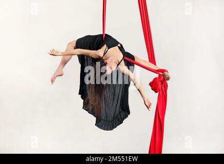 Ein ganzer Körper von anmutiger junger, barfüßiger Tänzerin, die auf roter Seide vor weißem Hintergrund einen Bogen aufführt Stockfoto