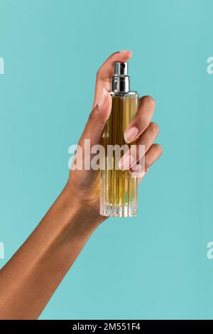 Anonyme afroamerikanische Frau sprüht aromatisches Parfüm aus Glasflasche vor türkisfarbenem Hintergrund Stockfoto