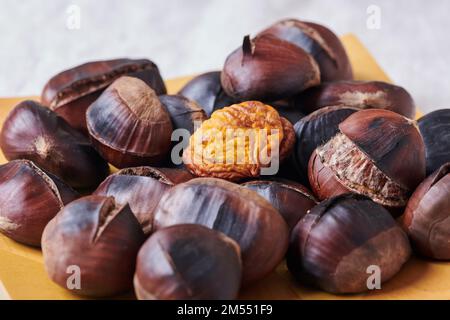 Ein Haufen köstlicher gerösteter Kastanien mit gerissenen Schalen, serviert auf Holzteller Stockfoto