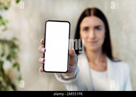 Weiche Fokussierung einer jungen Unternehmerin, die während der Arbeit im Büro ein Mobiltelefon mit leerem Bildschirm vorführt Stockfoto