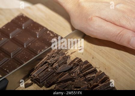 Eine Nahaufnahme eines Küchenchefs, der Schokoriegel mit einem Messer auf einem Schneidebrett in Stücke hackt Stockfoto