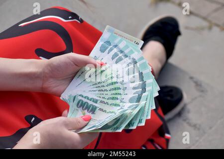 Ein Blick von oben auf weibliche Hände in rotem Kleid, die viele armenische Tausend Drachenscheine halten und zählen Stockfoto