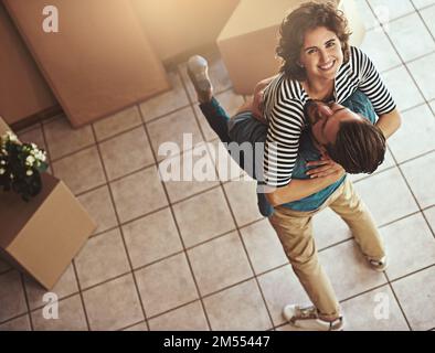 Unser Traum wurde wahr. Ein glückliches junges Paar, das sich umarmt, während sie in sein neues Zuhause ziehen. Stockfoto