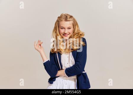 Lächelnde, wunderschöne, stilvolle, junge blonde Frau mit Retro-Frisur in Vintage-Outfit, isoliert auf grauem Hintergrund. Emotionen, Gesicht Stockfoto