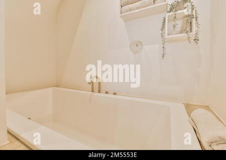 Eine weiße Badewanne in der Ecke des Badezimmers mit Pflanzen an der Wand und Handtüchern, die darüber hängen Stockfoto